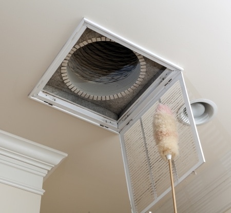 dusting the vent for air conditioning filter in ceiling of modern home