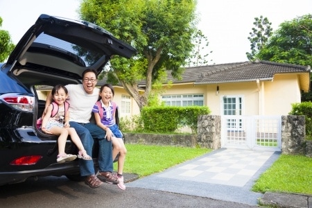 happy family sitting in the car and their house behind