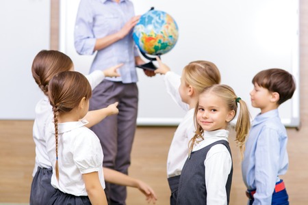geography practice. group of little school kids looks excided and pointing at the globe their teacher holding.