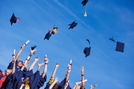 high school students graduates tossing up hats over blue sky.